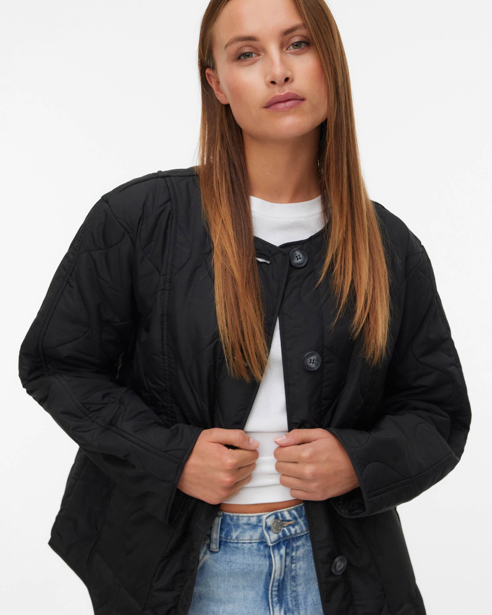 Woman wearing a black jacket over a white shirt and blue jeans on a white background